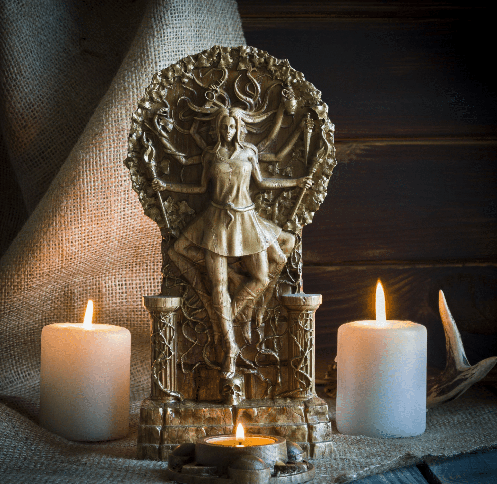 statue of a goddess surrounded by lit candles, creating a mystical and reverent atmosphere. The statue depicts the goddess with multiple arms holding various objects, symbolizing power and protection. The background features a rustic burlap cloth, and antlers are placed nearby, adding to the natural and earthy setting. The warm candlelight enhances the intricate details of the statue, emphasizing its spiritual significance.
