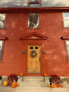 A bright red house in Salem, Massachusetts, with pumpkins and autumn decorations on the stone steps leading up to a wooden front door adorned with a wreath.