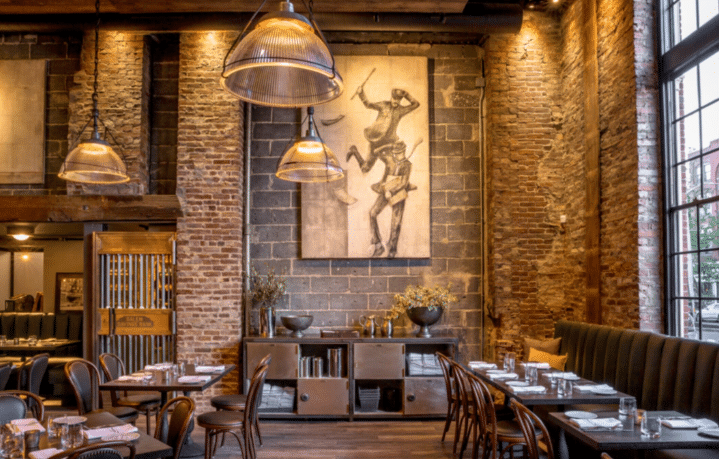 he interior of Ledger Restaurant in Salem, Massachusetts, featuring exposed brick walls, warm lighting, stylish modern artwork, and an inviting mix of contemporary and historic decor with neatly set tables.