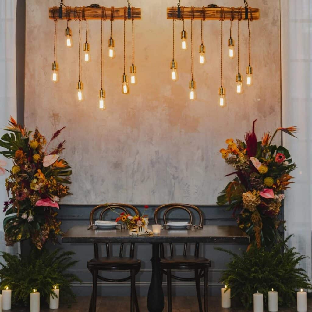 A beautifully decorated table setup at Ledger Restaurant in Salem, Massachusetts, featuring elegant hanging Edison bulb lighting, vibrant floral arrangements, and candle accents. This intimate and stylish setting is perfect for romantic dinners, special occasions, or private events, showcasing Ledger's attention to detail and charm.