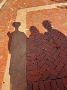 Shadows of three people dressed as the Sanderson Sisters from "Hocus Pocus" cast on a red brick pathway in Salem, Massachusetts.