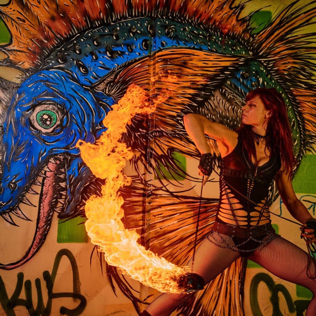 A fire performer in Salem Massachusetts spinning a flaming staff in front of a colorful mural at the Frozen Fire Festival.