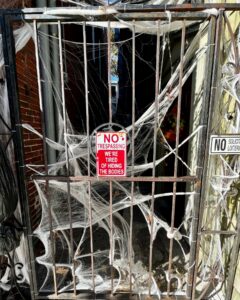 A gated alley in Salem decorated with spider webs and a humorous sign that reads "NO TRESPASSING: WE'RE TIRED OF HIDING THE BODIES," adding a spooky and playful vibe to the scene.