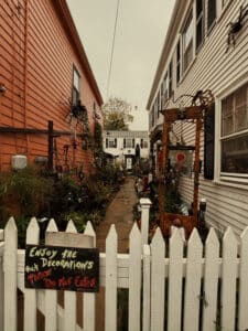 An alleyway between two houses, decorated for Halloween with various spooky decorations, plants, and a white picket fence at the entrance, with a sign that reads, "Enjoy the decorations, please do not enter." Salem Massachusetts