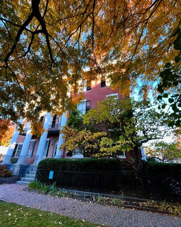 The Andrew-Safford House in Salem Massachusetts, partially obscured by golden autumn foliage, showcasing its Federal-style brick architecture and grand white columns.