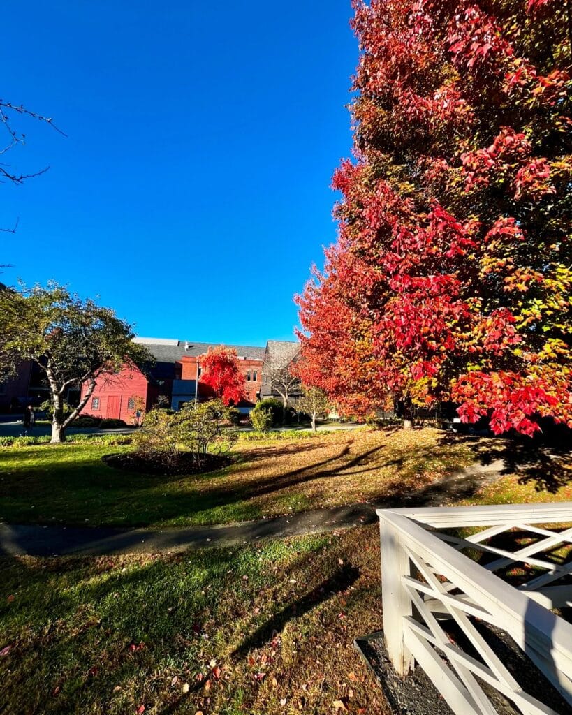 The Quaker Meeting House in Salem, Massachusetts, surrounded by vibrant autumn foliage, with bright red and orange leaves contrasting against the clear blue sky and historic architecture.