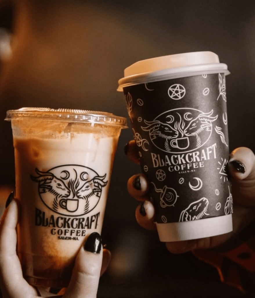 Two coffee cups from Blackcraft Coffee in Salem, Massachusetts, displaying gothic designs with celestial and horned imagery.