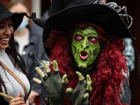 Borah, a costumed witch with green face paint and red hair, captivates visitors in Salem, Massachusetts, with her animated expressions and elaborate attire.