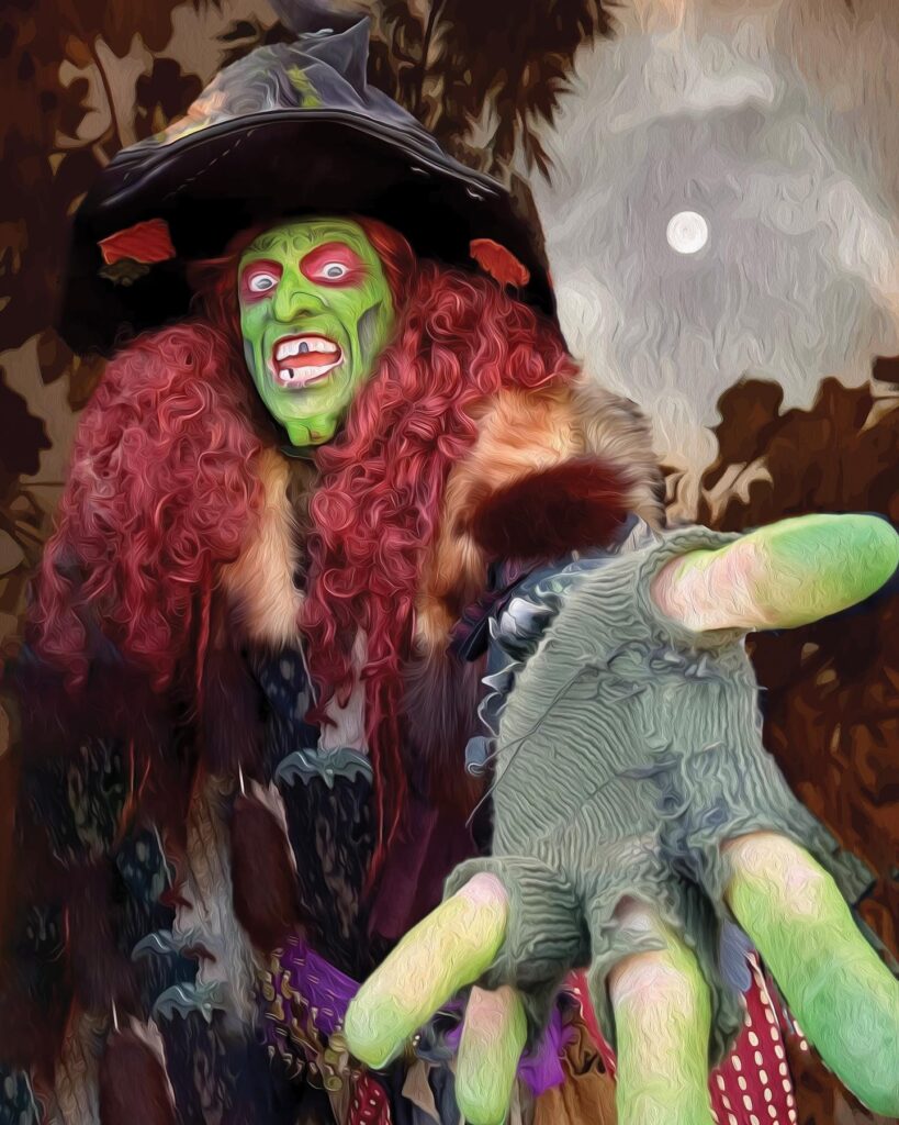 Borah, a witch with green face paint, red hair, and a dramatic costume, extends her hand toward the viewer under a glowing full moon in Salem, Massachusetts.