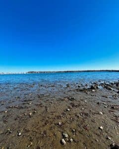 Shoreline of Salem Harbor in Salem, Massachusetts, with calm water, scattered rocks, and a clear blue sky.