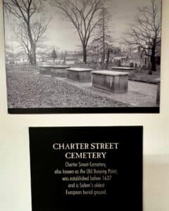 Black-and-white image of Charter Street Cemetery, also known as the Old Burying Point, in Salem, Massachusetts, showcasing above-ground tombs and gravestones among bare trees.