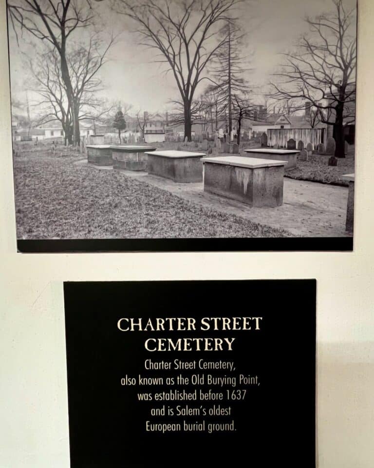 Black-and-white image of Charter Street Cemetery, also known as the Old Burying Point, in Salem, Massachusetts, showcasing above-ground tombs and gravestones among bare trees.