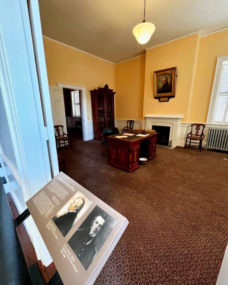The Collector's Office inside the Salem Custom House in Salem, Massachusetts, featuring period furnishings, a historic desk, a fireplace, and portraits displayed on a placard in the foreground.