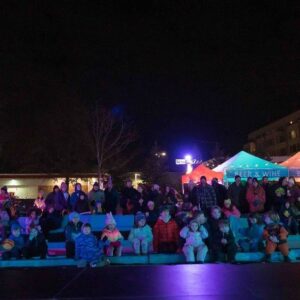 A nighttime view of families seated at the Frozen Fire Festival in Salem, Massachusetts, with colorful tents and festive lighting illuminating the scene.