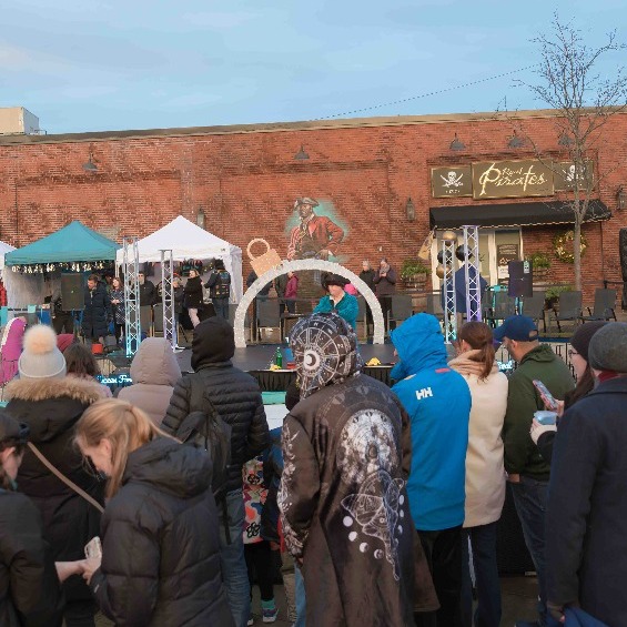 A lively crowd gathers at the Salem Frozen Fire Festival, featuring a pirate-themed mural, vendor tents, and a stage in Salem, Massachusetts.