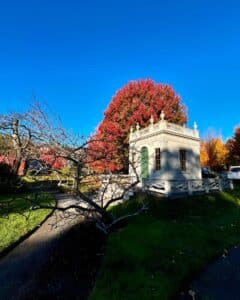 The Derby-Beebe Summer House in Salem, Massachusetts, framed by vivid red autumn leaves and surrounded by a peaceful garden path.