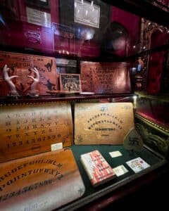A showcase featuring vintage Ouija boards, including designs with unique markings, and mystical artifacts at the Salem Witch Board Museum in Salem, Massachusetts.