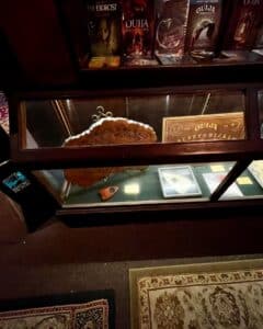 A glass display case at the Salem Witch Board Museum showcasing vintage Ouija boards and planchettes, accompanied by horror-themed DVDs like "The Exorcist" and "Ouija: Origin of Evil."