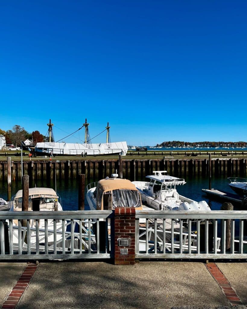 Boats docked at the Salem waterfront in Massachusetts with the Friendship of Salem, a historical ship, in the background under a clear blue sky.