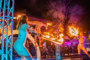 Two performers wield flaming staffs while a third balances in an intricate pose during an electrifying nighttime show in Salem, Massachusetts.