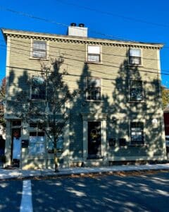 David Ropes House in Salem, Massachusetts, featuring a three-story green wooden structure with intricate detailing and a welcoming black door adorned with a sunflower wreath.