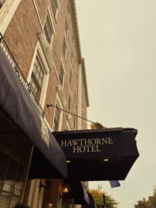 A side view of the Hawthorne Hotel with its classic blue awning and brick facade, set against a pale sky. Salem Massachusetts