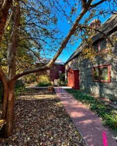 The pathway leading to the Old Burying Point Charter Street Cemetery Welcome Center in Salem Massachusetts, surrounded by autumn leaves, trees, and colonial-style architecture.