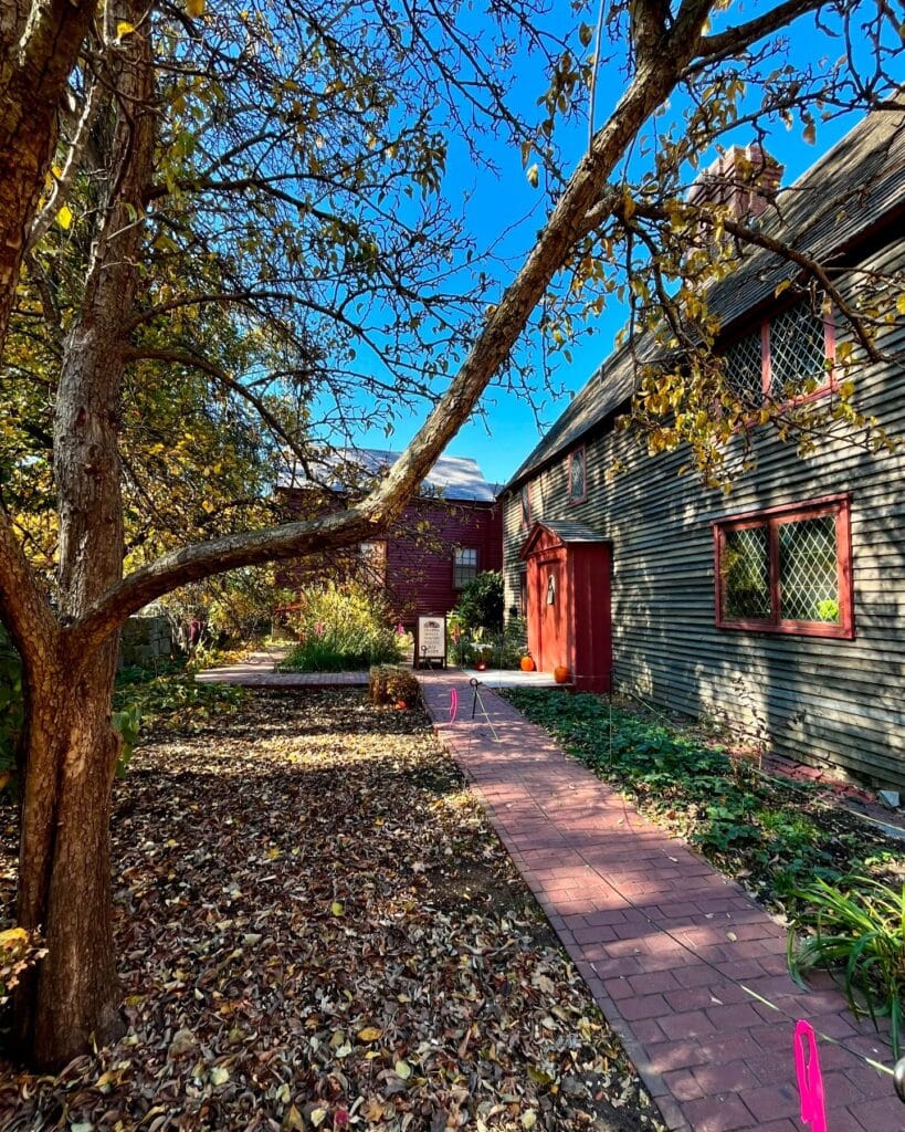 The pathway leading to the Old Burying Point Charter Street Cemetery Welcome Center in Salem Massachusetts, surrounded by autumn leaves, trees, and colonial-style architecture.