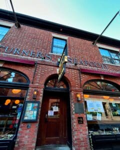 The entrance to Turner's Seafood in Salem Massachusetts, showcasing its red brick facade, arched windows, and hanging gold sign.