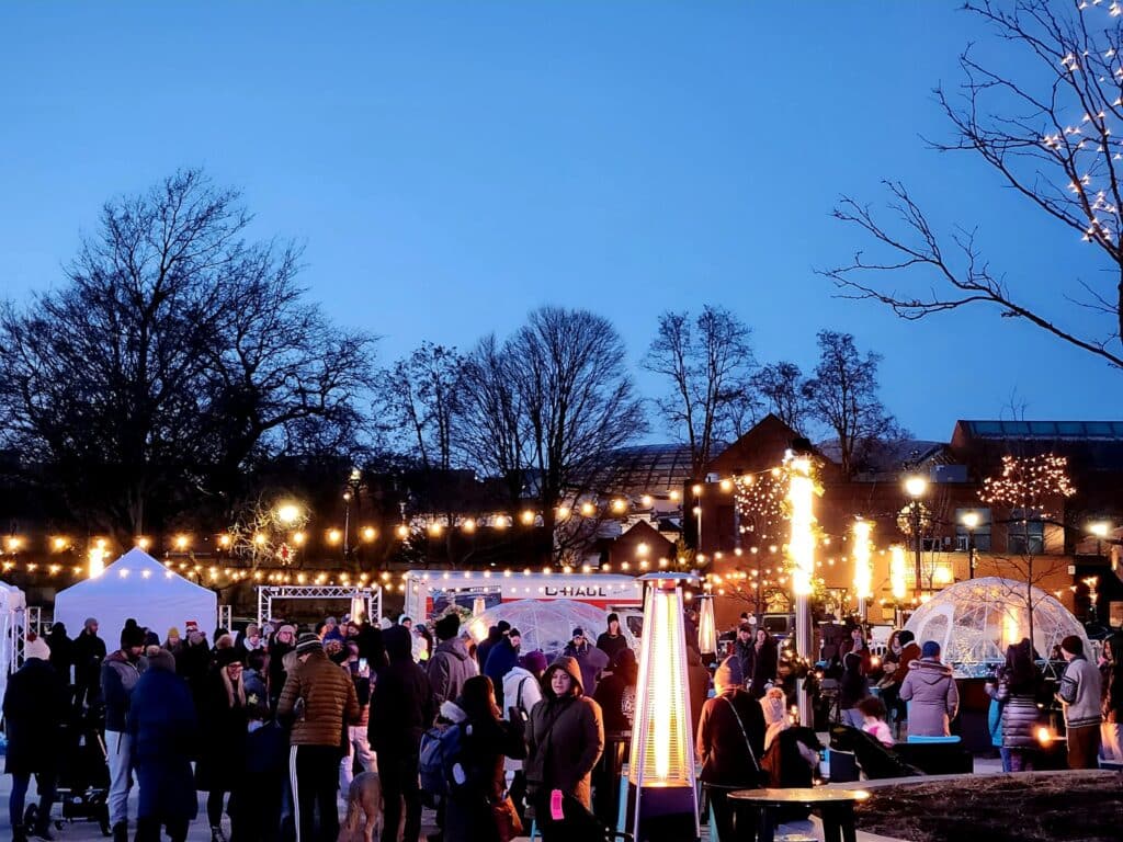 People gathered under glowing lights at the Salem Massachusetts Frozen Fire Festival, visiting heated tents and enjoying warm conversations on a crisp winter evening.