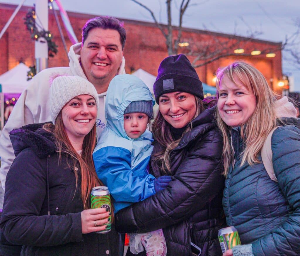 A group of friends and family in Salem Massachusetts, including a bundled-up toddler, smiling together at the Frozen Fire Festival.