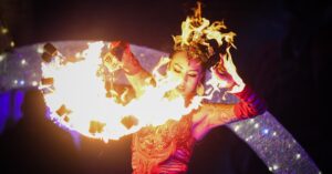 A performer in Salem Massachusetts dressed in intricate red attire, manipulating flaming props with precision and grace during the Frozen Fire Festival.