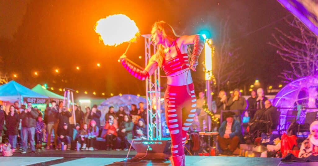 A performer in Salem Massachusetts dressed in red, spinning flaming props on stage under vibrant lights at the Frozen Fire Festival.
