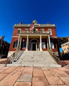 Straight-on view of the Salem Custom House in Salem, Massachusetts, showcasing its grand staircase, Federal-style design, and iconic golden eagle under a bright blue sky.