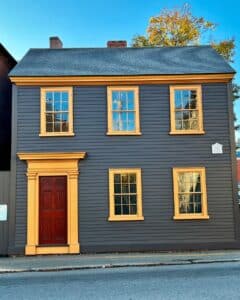 The Daniel Bray House in Salem, Massachusetts, features dark wood siding, golden window and door trim, and a distinct historical plaque from 1766.