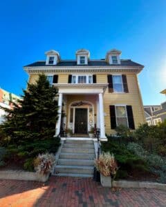 The front facade of the John P. Peabody House in Salem Massachusetts, featuring a grand staircase, white columns, and a yellow exterior with classic black shutters.