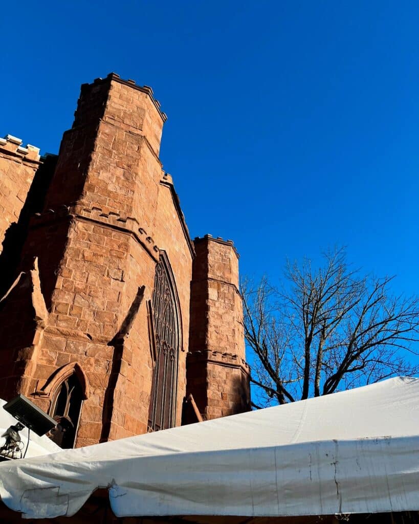 The towering stone structure of the Salem Witch Museum, featuring gothic architectural details like pointed arches and battlements, set against a vibrant blue sky with part of a white tent in the lower section.