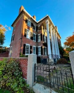 Andrew-Safford House in Salem Massachusetts with a decorative iron gate in the foreground, featuring Federal-style architecture with large white columns and a brick exterior.