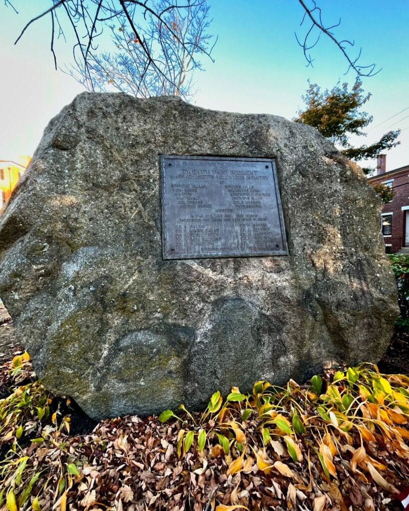 A granite stone memorial with a plaque commemorating the Twenty Third Regiment in Salem, Massachusetts, surrounded by autumn leaves.