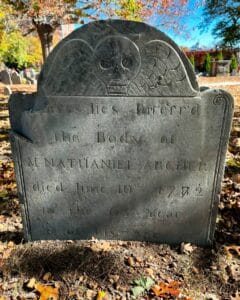 lose-up of a gravestone in Salem Massachusetts's Old Burying Point cemetery for Mr. Nathaniel Archer, who passed in 1782, featuring a winged skull carving symbolizing mortality and a detailed inscription.