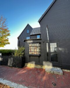 The House of the Seven Gables in Salem, Massachusetts, highlighting its dark wooden siding, bay window, and brick pathway under a clear sky.