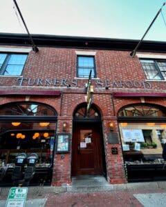 Close-up of the historic brick entrance of Turner's Seafood in Salem Massachusetts, featuring arched windows, a wooden door, and illuminated lanterns.