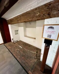 Interior of the Pickman House in Salem, Massachusetts, showing a brick-lined floor and white brick alcoves, with a sign indicating reservations are required for Charter Street Cemetery visits.