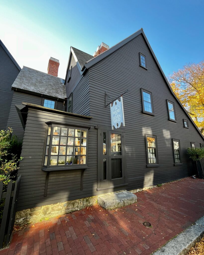 The historic House of the Seven Gables in Salem, Massachusetts, showcasing dark wood siding, a steep roof, and a sign marking its significance.