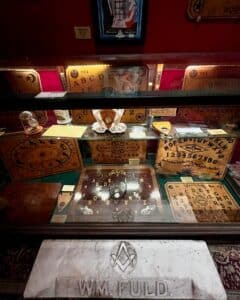 A display case at the Salem Witch Board Museum in Salem, Massachusetts, featuring vintage Ouija boards, a Masonic W.M. Fuld marker, and various spiritual communication artifacts.