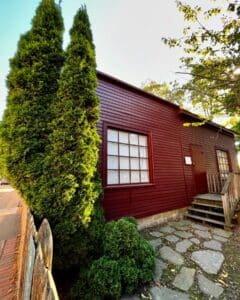 A historic red wooden building near the Old Burying Point Cemetery in Salem, Massachusetts, with a stone pathway, large window, and wooden steps leading to the entrance.