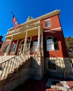 Front view of the Salem Custom House in Salem, Massachusetts, featuring a grand staircase, columns, and a golden eagle ornament under a clear blue sky.