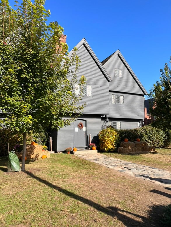 The Witch House in Salem, Massachusetts, decorated for Halloween with pumpkins, bales of hay, and a wreath on the door, under a bright blue sky.