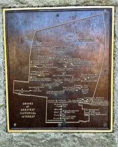 A bronze map plaque in Salem Massachusetts's Old Burying Point Cemetery detailing graves of historical significance, including names like Nathaniel Bowditch, Mary Corry, and Simon Bradstreet, with inscriptions and an engraved layout of the burial sites.