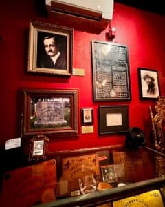 A wall display featuring historical portraits, text panels, and a photo of an engraved tombstone alongside vintage Ouija boards in a glass case at the Salem Witch Board Museum in Salem, Massachusetts.